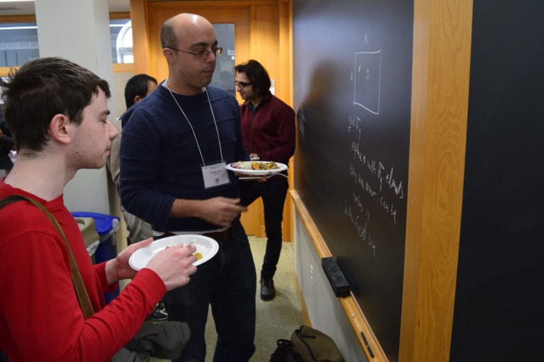 two guys looking at the problem in black-board while eating